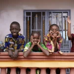 Five African Children Greeting Bypassers From A Colonial House Balcony