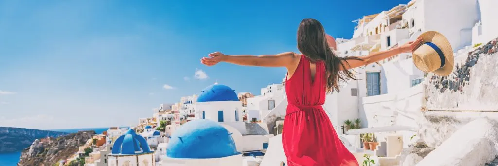 Europe travel vacation fun summer woman feeling free dancing with arms open in freedom at Oia, Santorini, Greece island. Carefree girl tourist banner panorama.